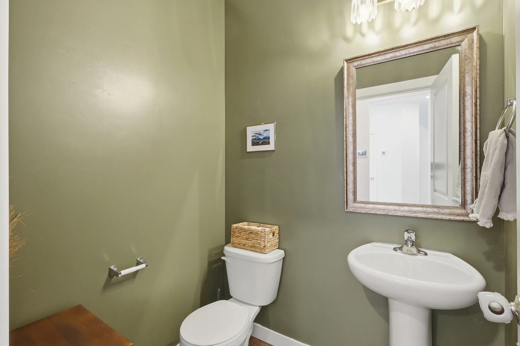Pedestal sink with a polished chrome faucet, framed mirror, and a wall-mounted light fixture
