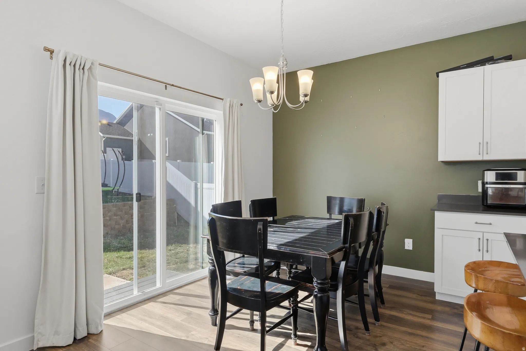 Wood-finish flooring, sliding glass door, overhead chandelier, white cabinetry, and a dark countertop