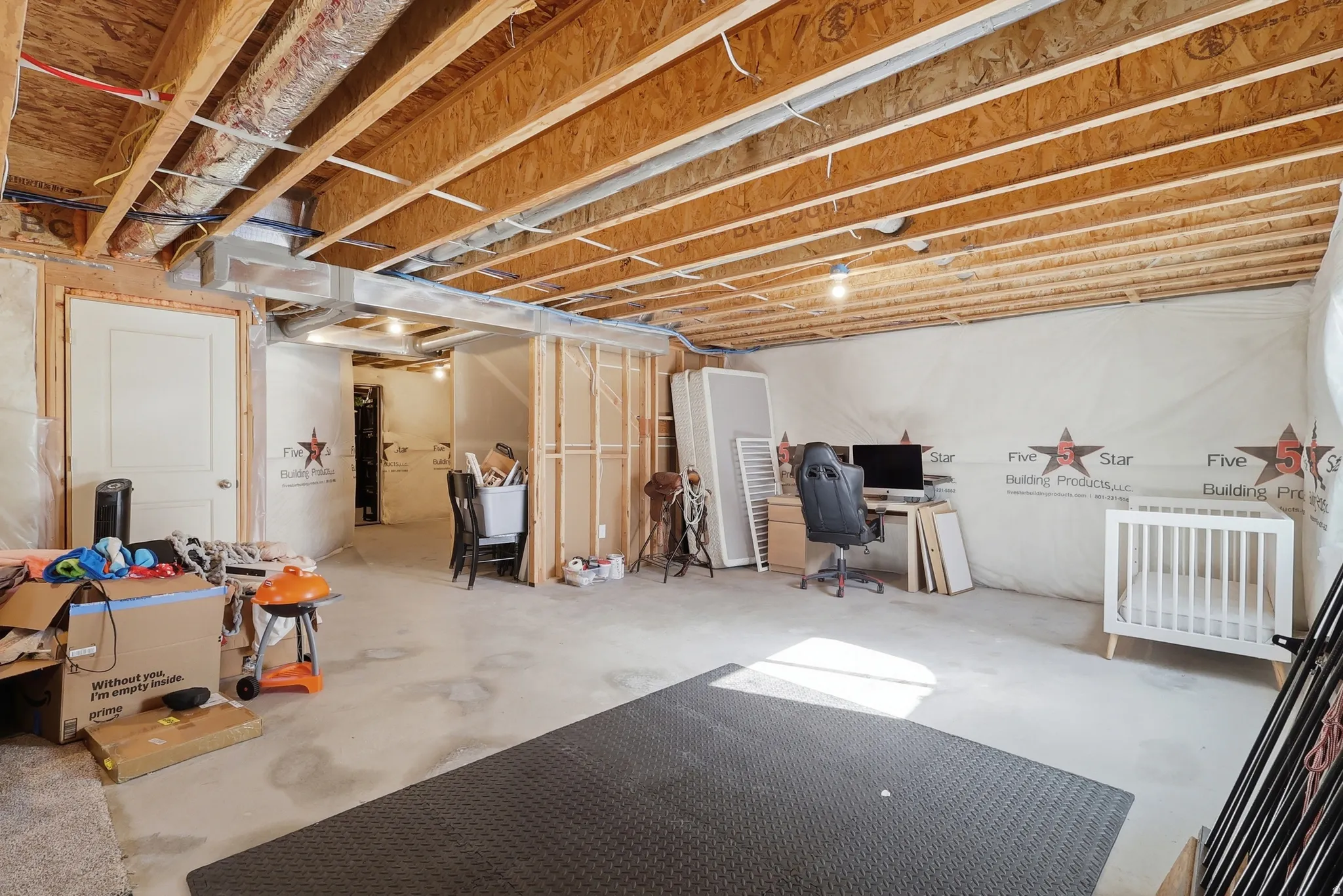 Unfinished basement space with exposed wood joists and concrete flooring, featuring framed wall sections and an interior door