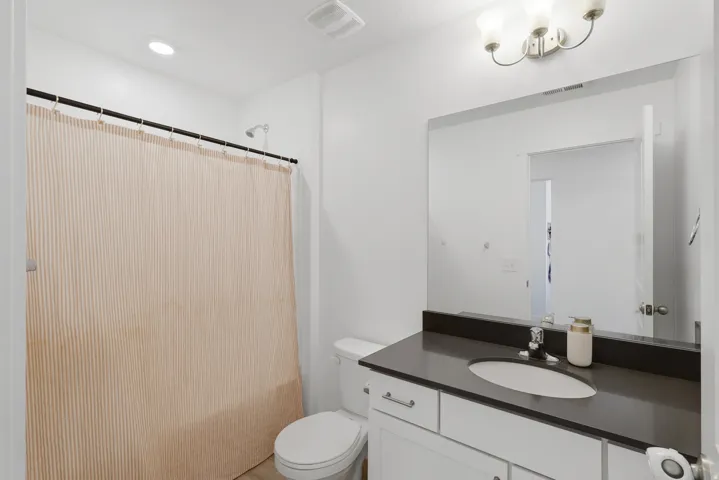 Vanity with a dark countertop and undermount sink, large wall-mounted mirror, and a three-light fixture
