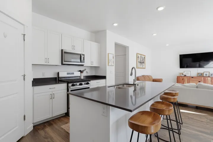 Recessed lighting illuminates a kitchen featuring white cabinetry, dark countertops, and stainless steel appliances