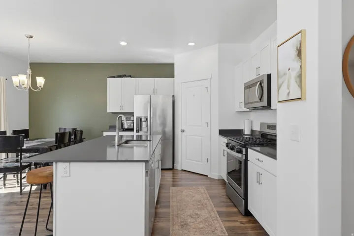 Kitchen featuring a central island with an undermount sink, white cabinetry, dark countertops, and stainless steel appliances