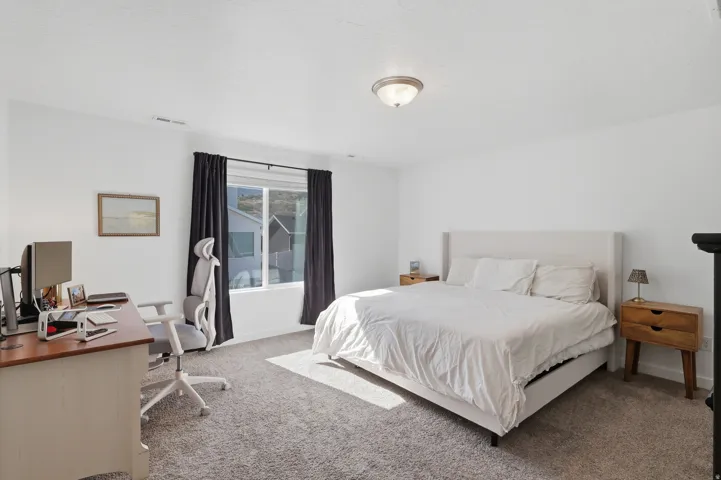 Neutral-toned carpeted flooring, white painted walls, and a large window with dark curtain rods and curtains