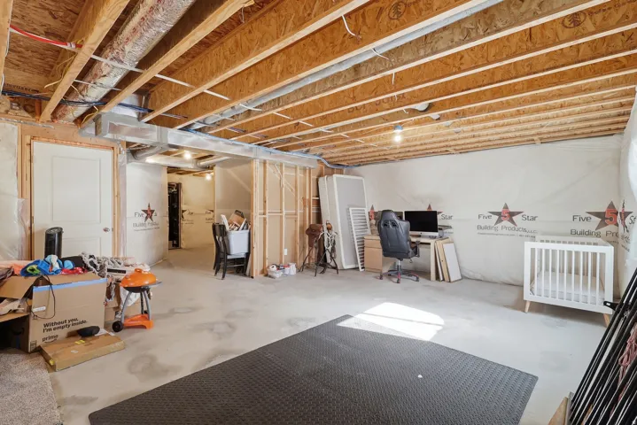 Unfinished basement space with exposed wood joists and concrete flooring, featuring framed wall sections and an interior door