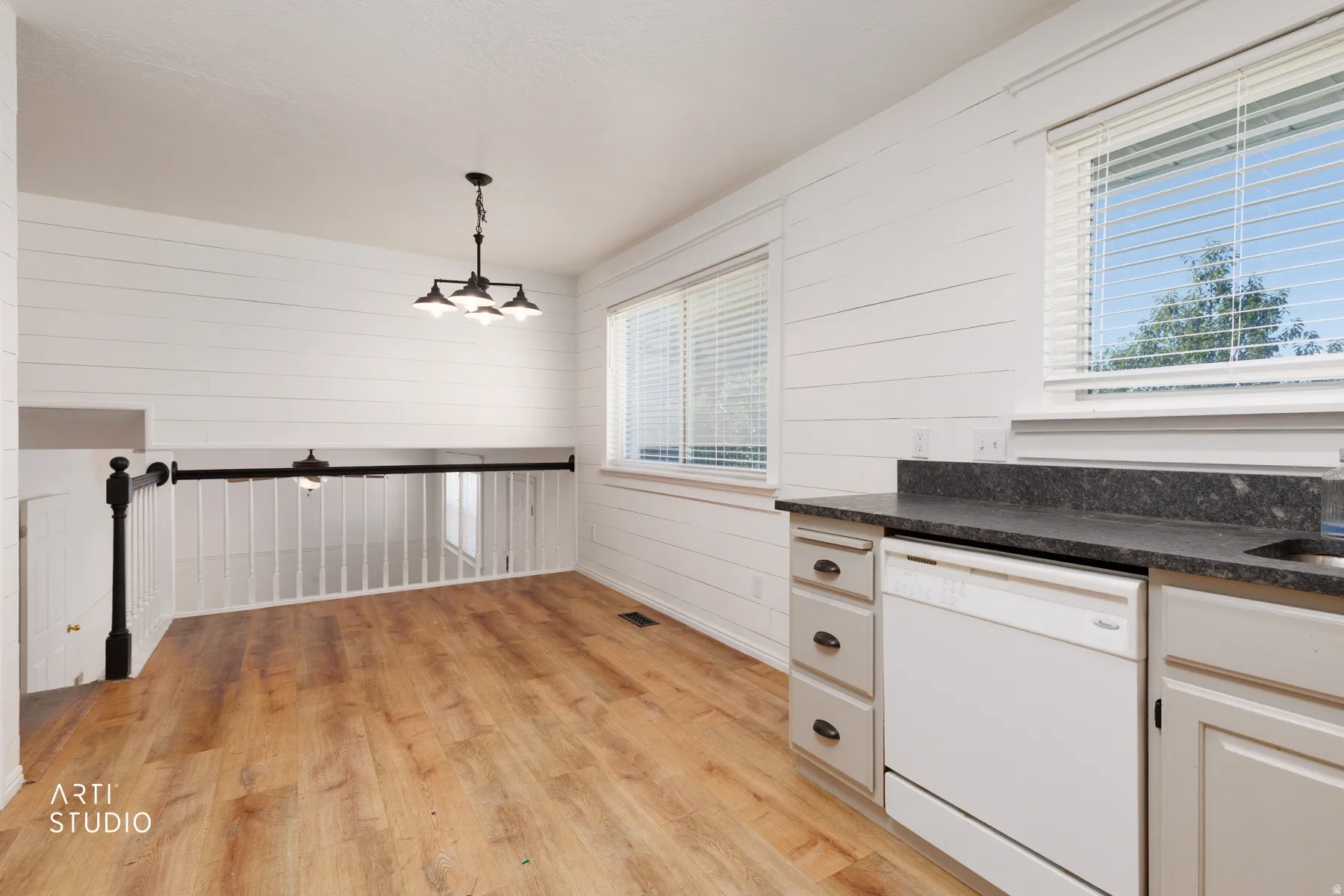 Wood-finish flooring, white shiplap walls, dark countertop, white cabinetry, and a black metal light fixture