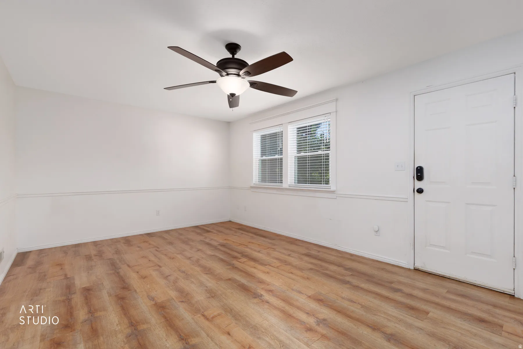 Wood-finish flooring, white walls with chair rail molding, multi-pane window, and a ceiling fan with integrated lighting