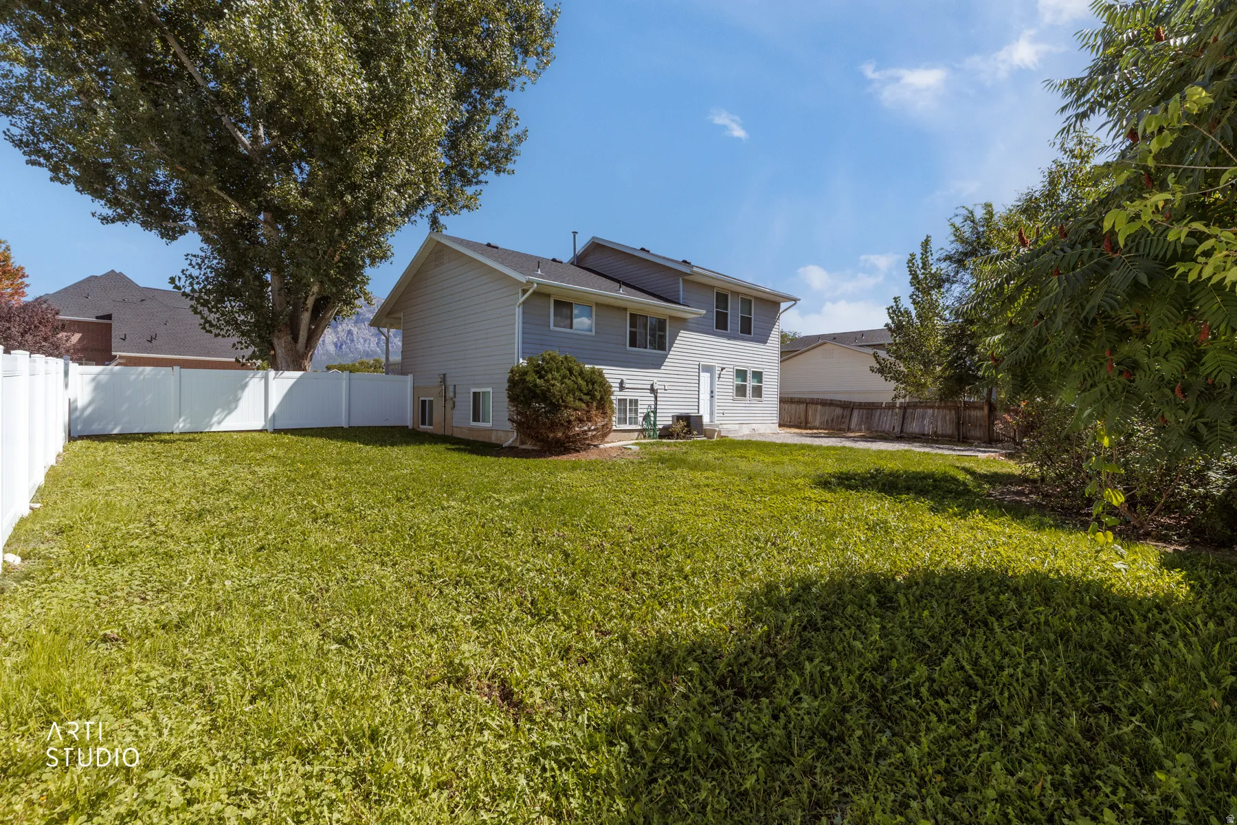 Expansive backyard with a manicured lawn, established trees, and a durable white vinyl fence