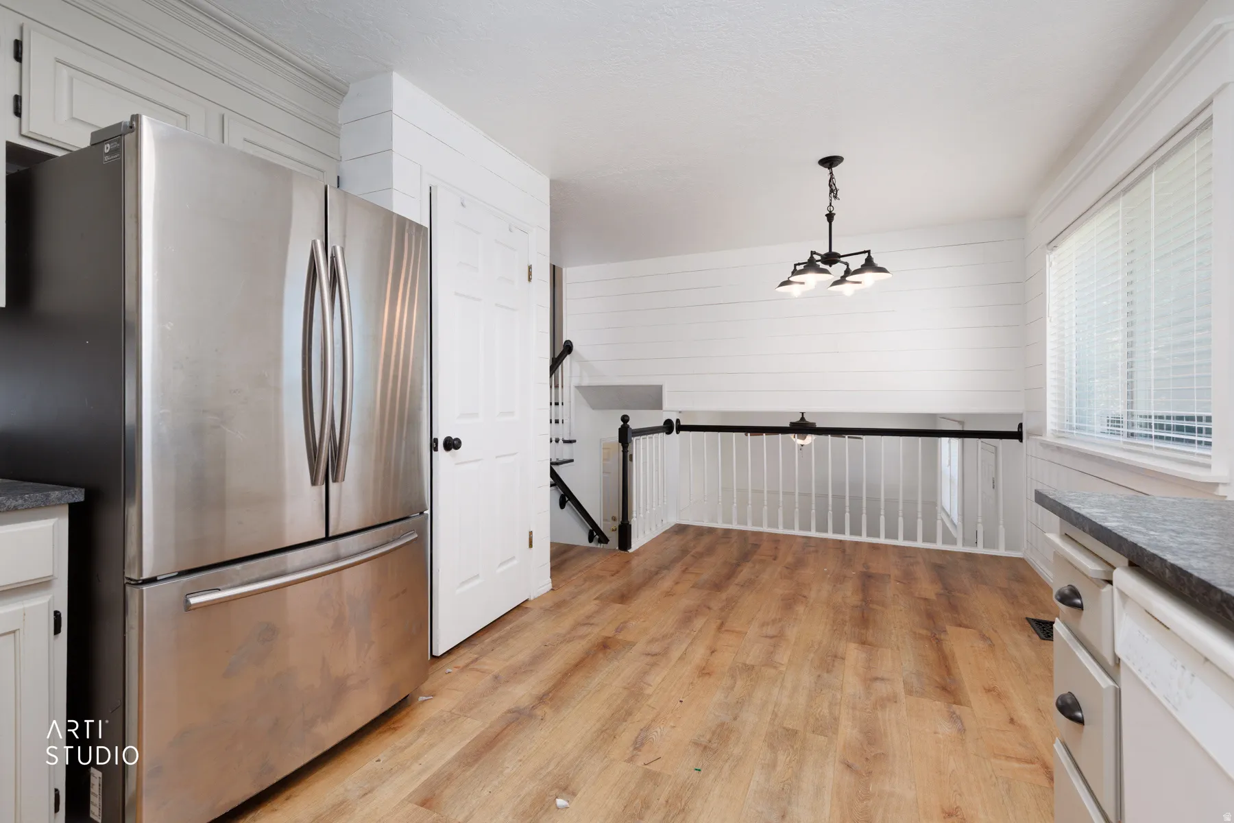 Stainless steel refrigerator, wood-finish flooring, white shiplap accent wall, white cabinetry with dark hardware, and a dark-finish chandelier