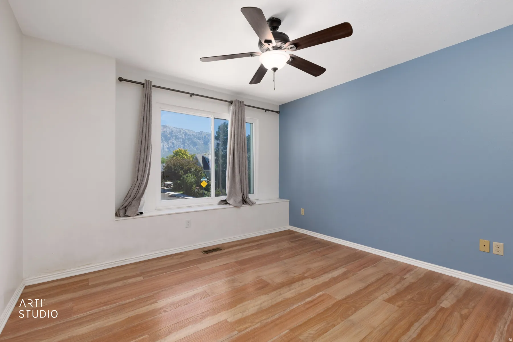 Wood-finish flooring, ceiling fan with integrated lighting, large window with window seat, and accent wall