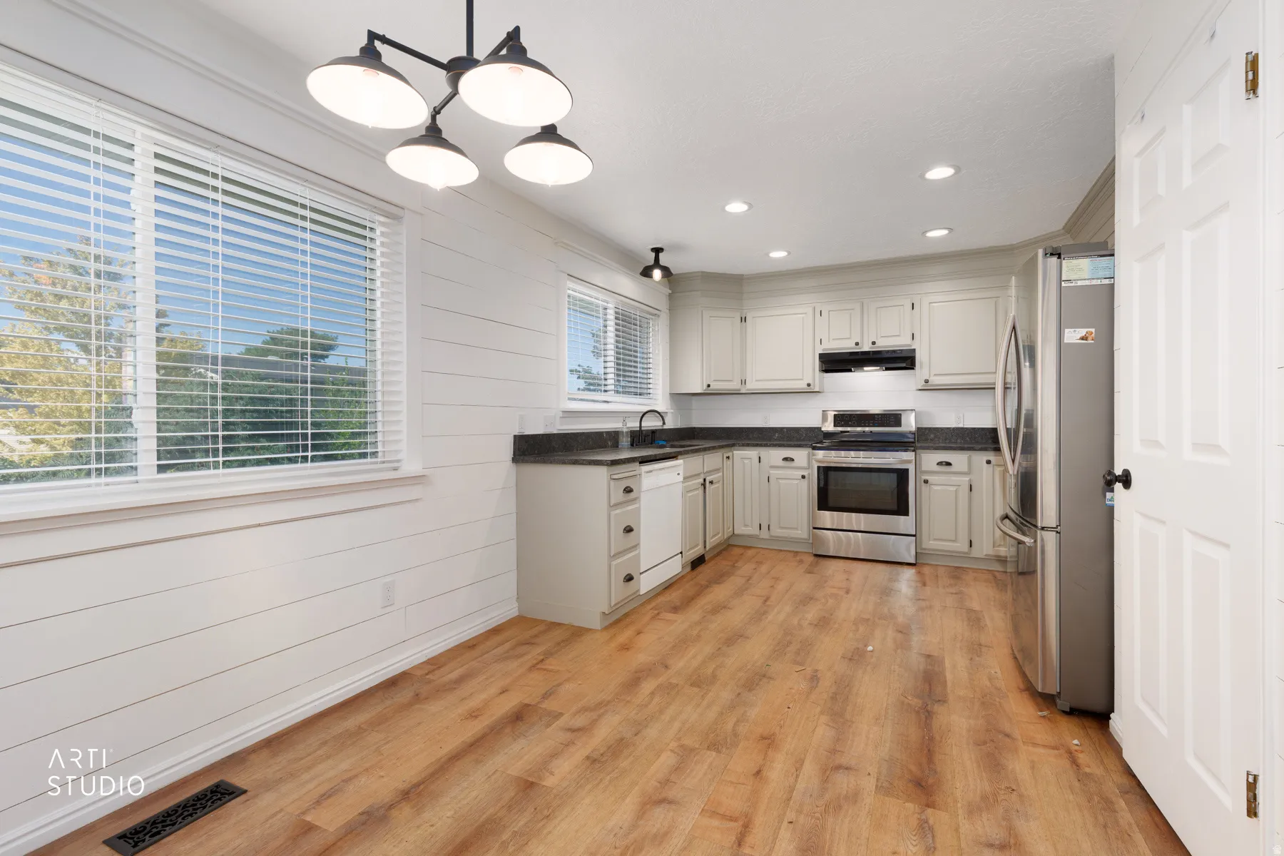 Kitchen featuring wood-finish flooring, white shaker-style cabinetry, stainless steel appliances, dark countertops, and recessed lighting