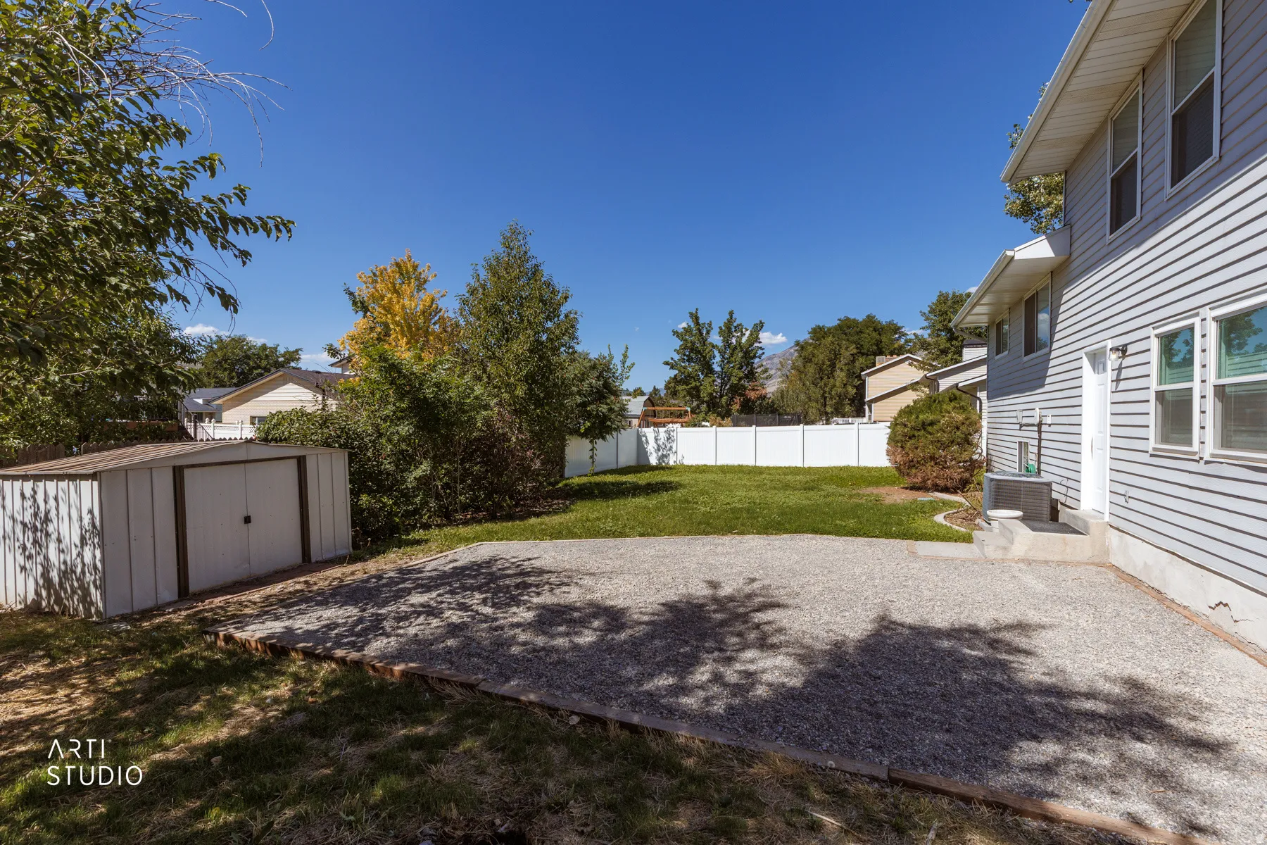 Expansive backyard featuring a gravel patio, manicured lawn, and mature trees