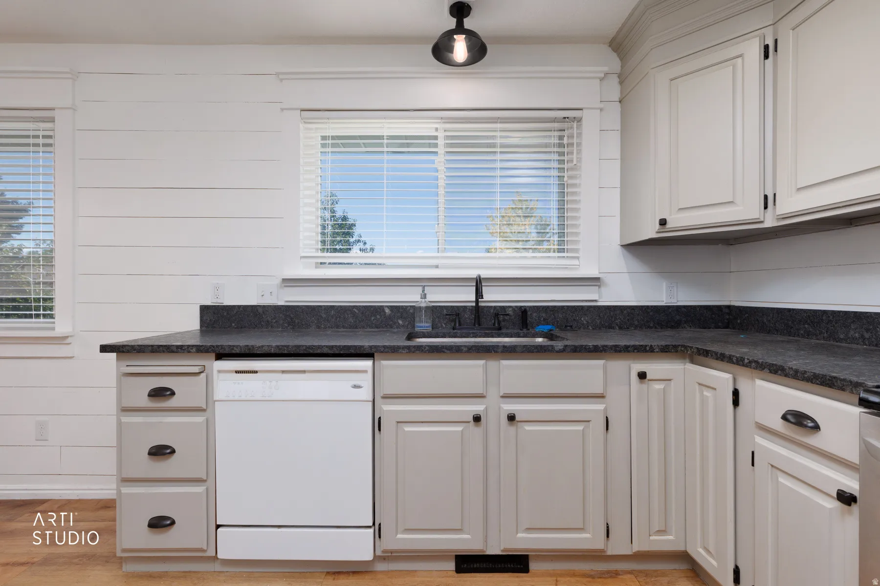 Kitchen featuring a corner sink, dark countertops, light-toned cabinetry, and wood-finish flooring