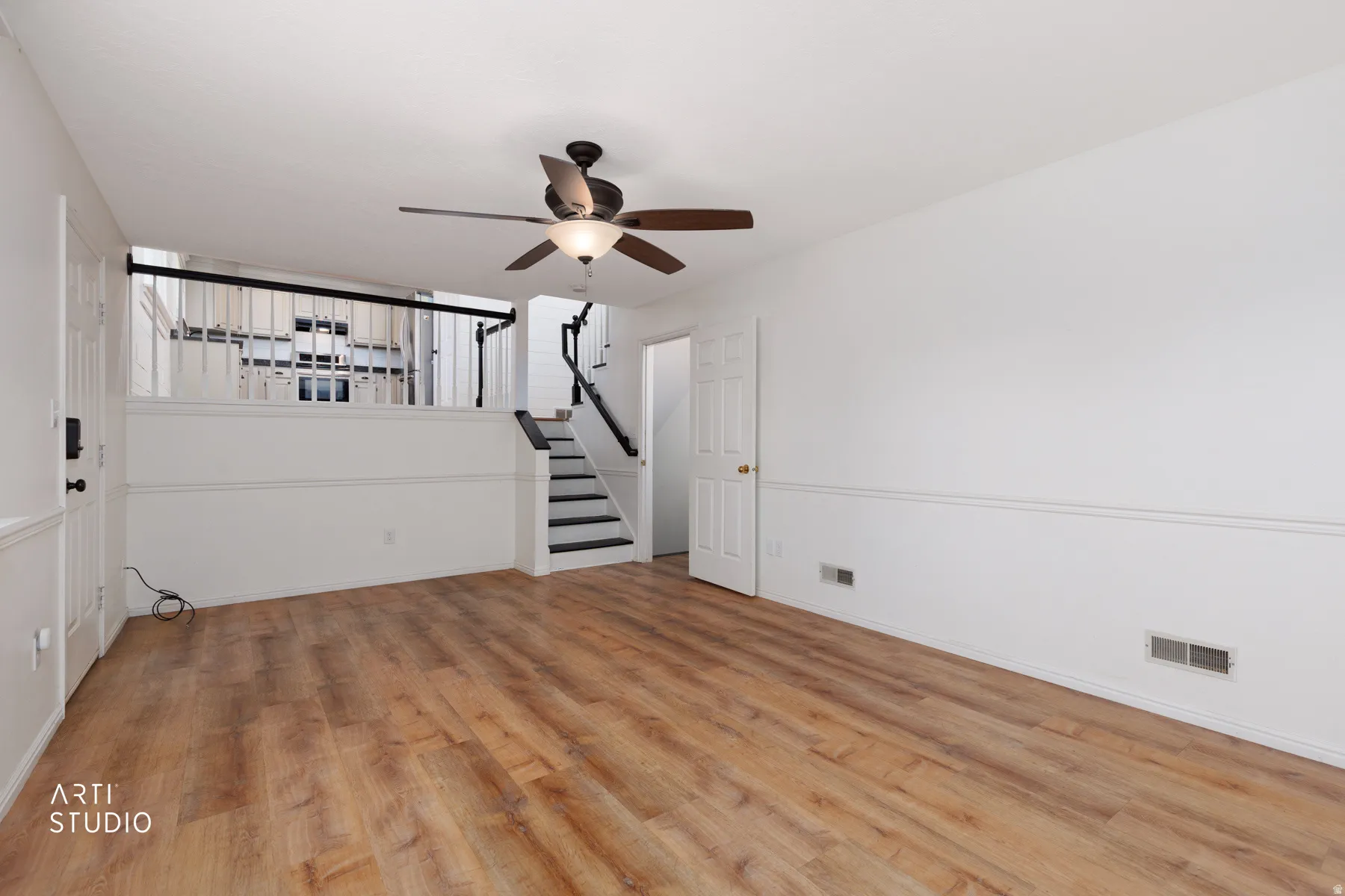 Expansive room featuring wood-finish flooring, a contemporary ceiling fan, and a built-in staircase with a black railing