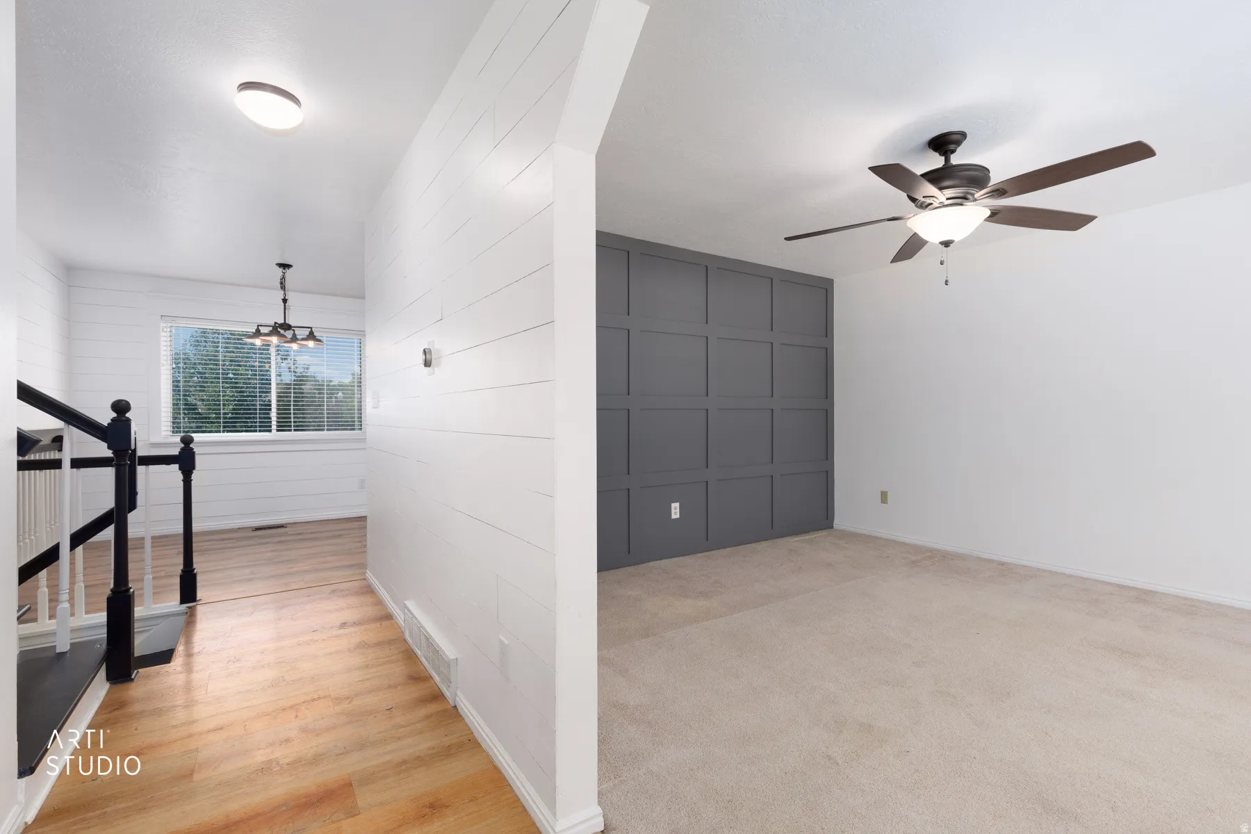 Shiplap accent wall, wood-finish flooring, ceiling fan, and staircase with black railing