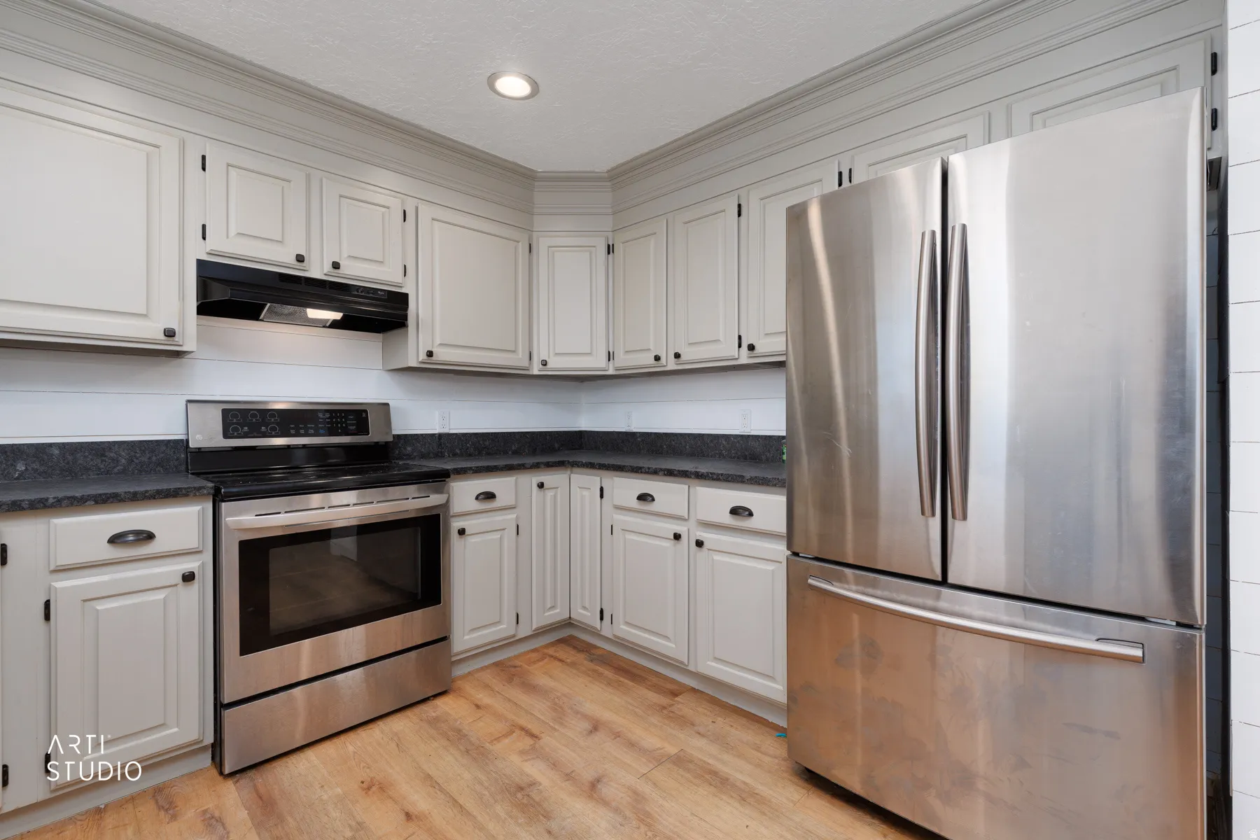 Kitchen featuring stainless steel appliances, light-toned cabinetry with dark hardware, dark countertops, and wood-finish flooring