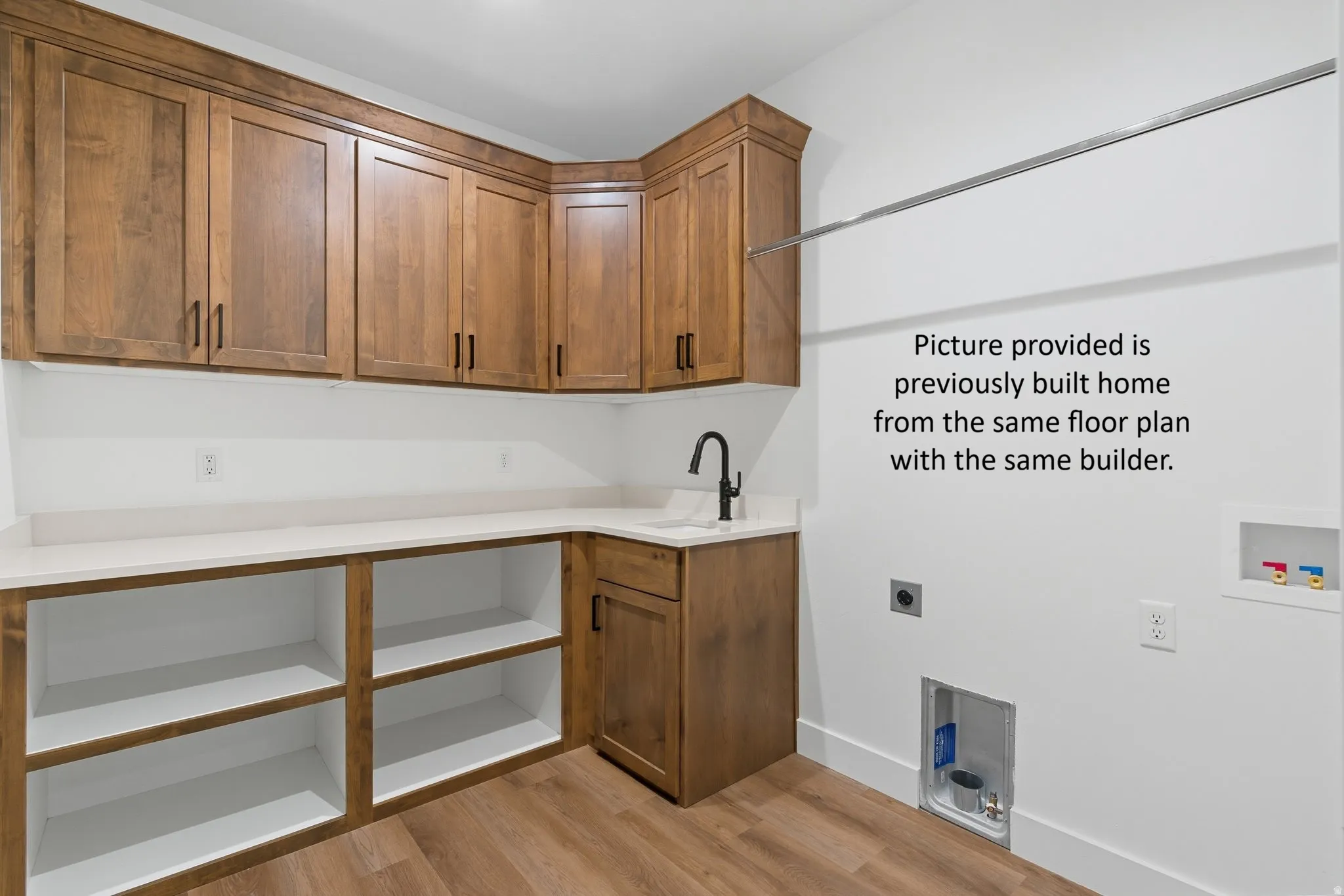 Wood-finish cabinetry, light-toned countertops, built-in shelving, wood-finish flooring, and a utility sink with a matte black faucet