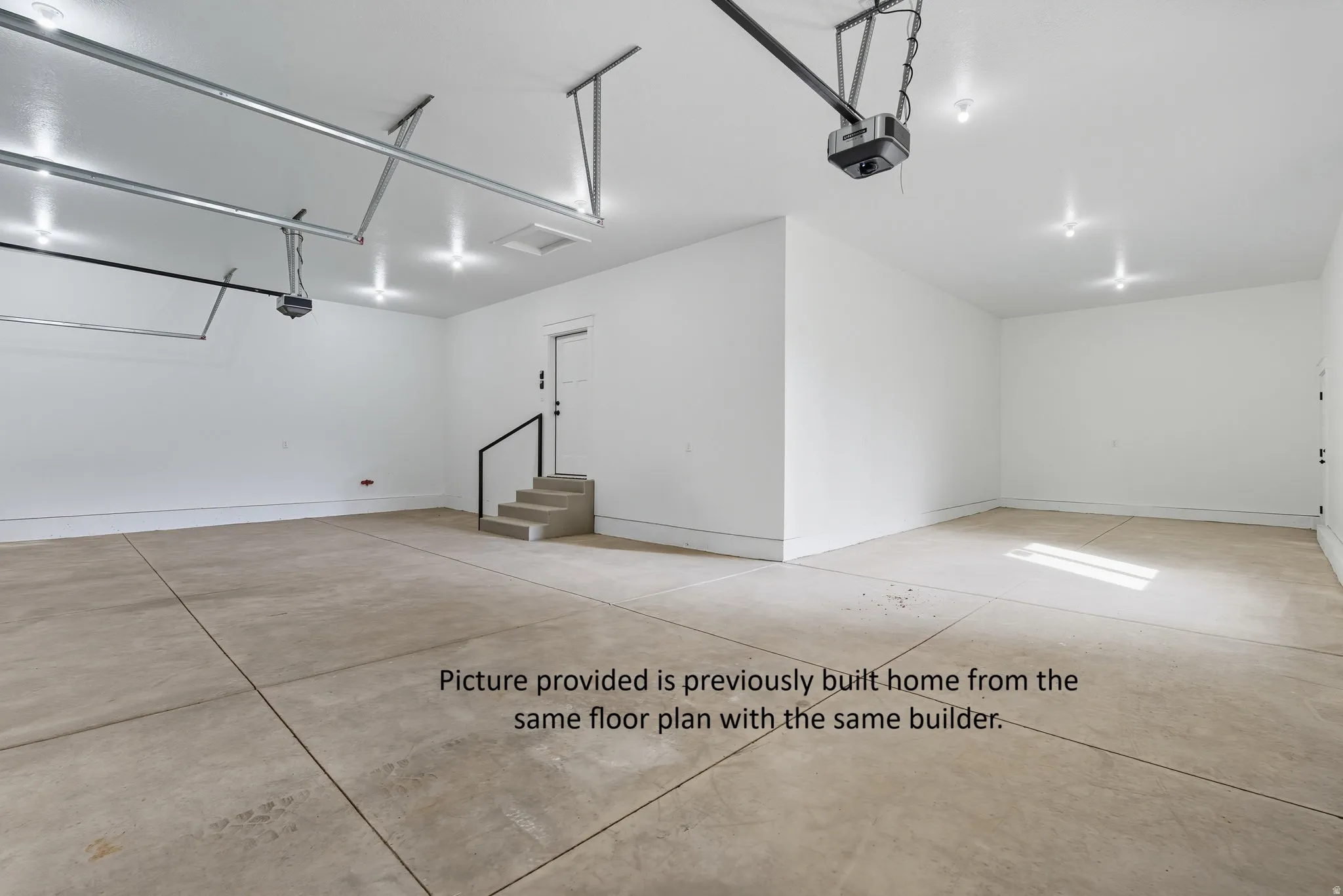 Spacious garage with exposed concrete flooring, recessed lighting, white walls, and a built-in concrete staircase with a black handrail