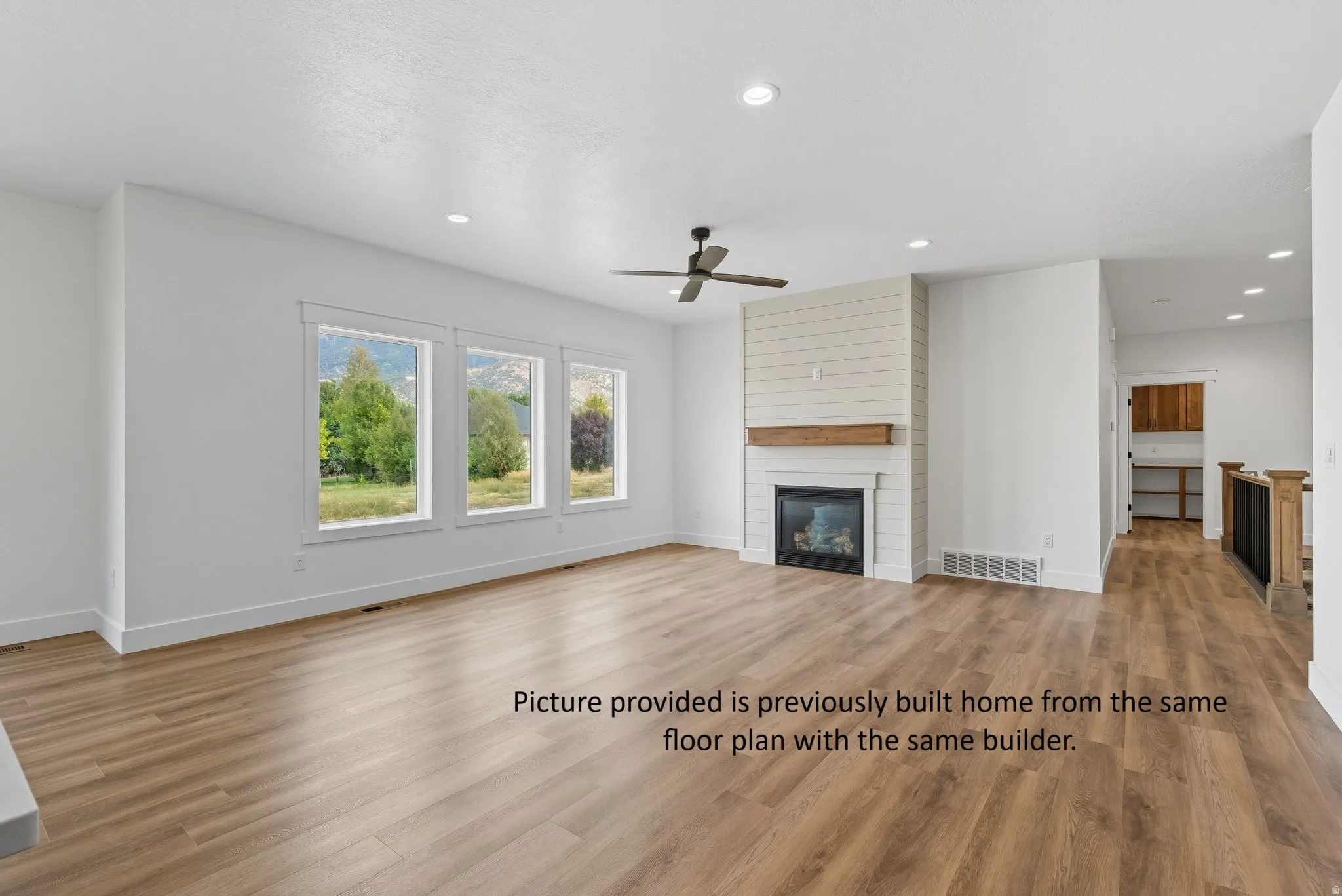 Spacious living area featuring wood-finish flooring, a contemporary fireplace with a shiplap accent wall, a solid wood mantel, and multiple windows