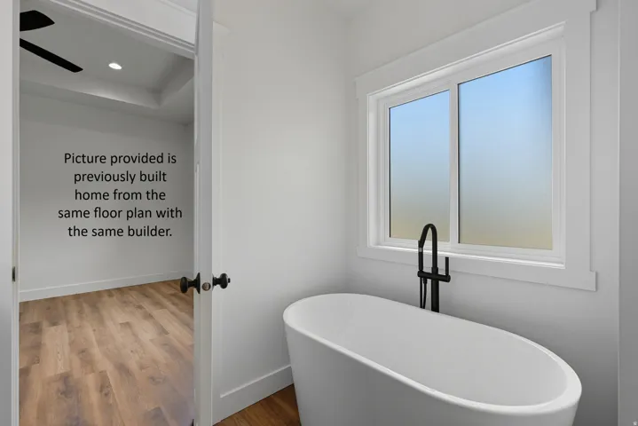 Freestanding bathtub with matte black floor-mounted faucet, white window trim, and wood-finish flooring