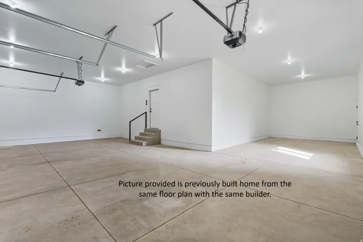Spacious garage with exposed concrete flooring, recessed lighting, white walls, and a built-in concrete staircase with a black handrail