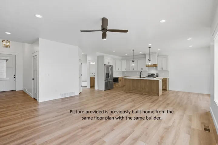Wood-finish flooring throughout, recessed ceiling lighting, kitchen island with pendant lighting, white cabinetry, and stainless steel appliances