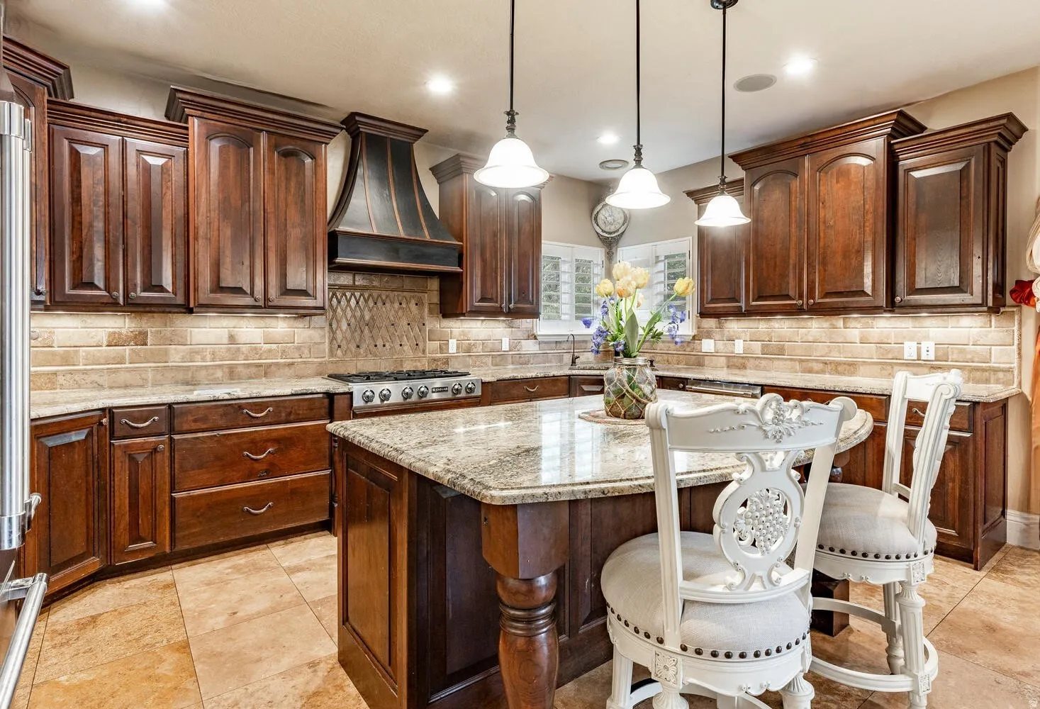 Gourmet kitchen featuring rich wood cabinetry, granite countertops, a built-in gas range with a custom range hood, a spacious central island, and stone tile flooring