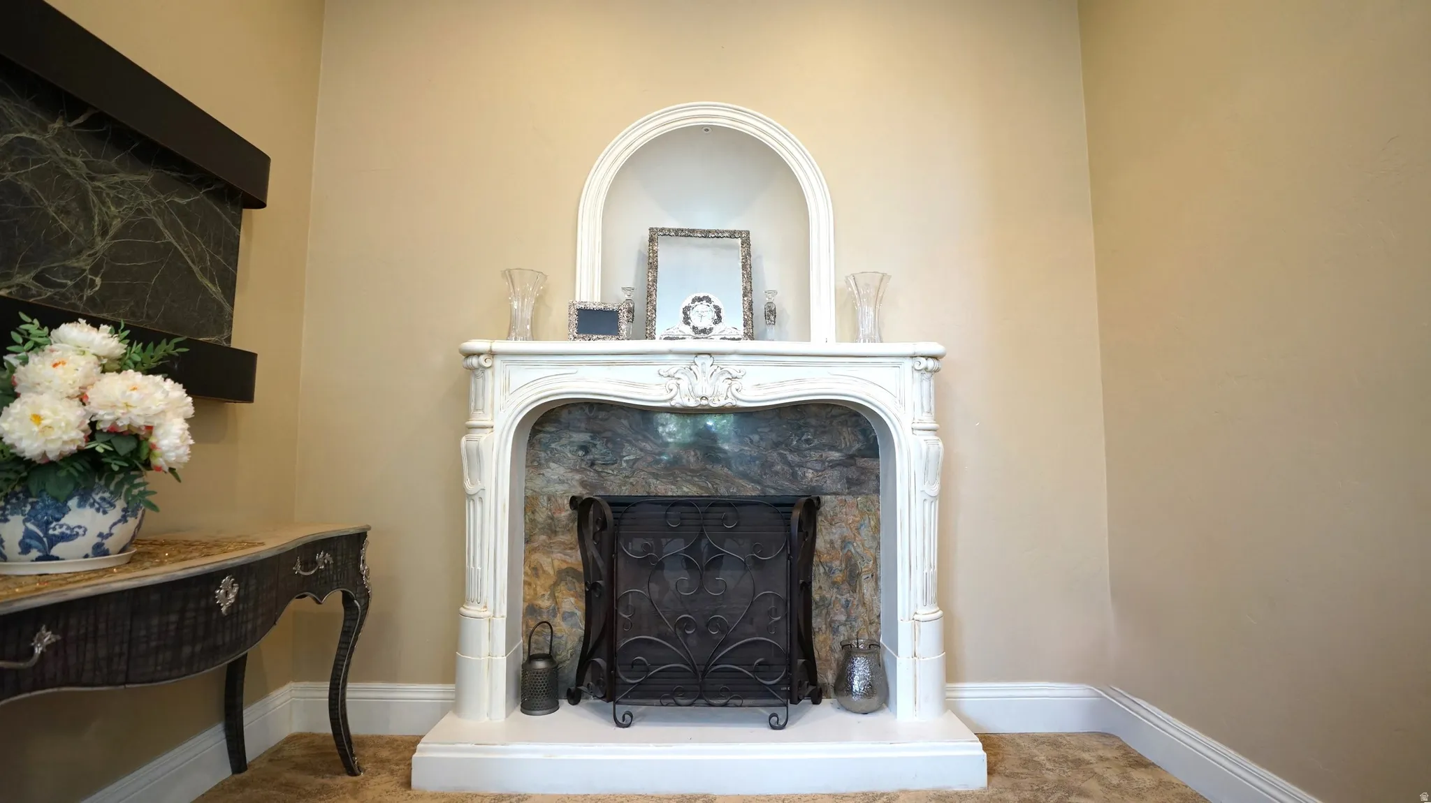 Ornate white fireplace surround with a dark stone-finish firebox, complemented by an arched niche