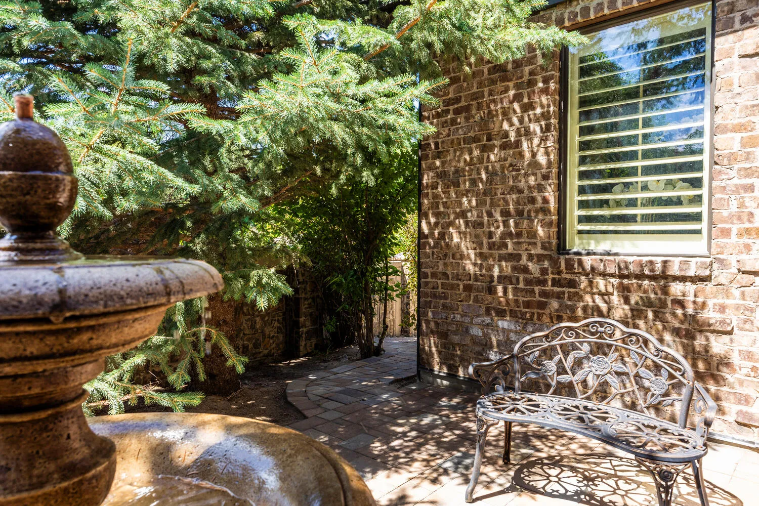 Brick exterior, paver walkway, mature evergreen landscaping, and a window with horizontal blinds