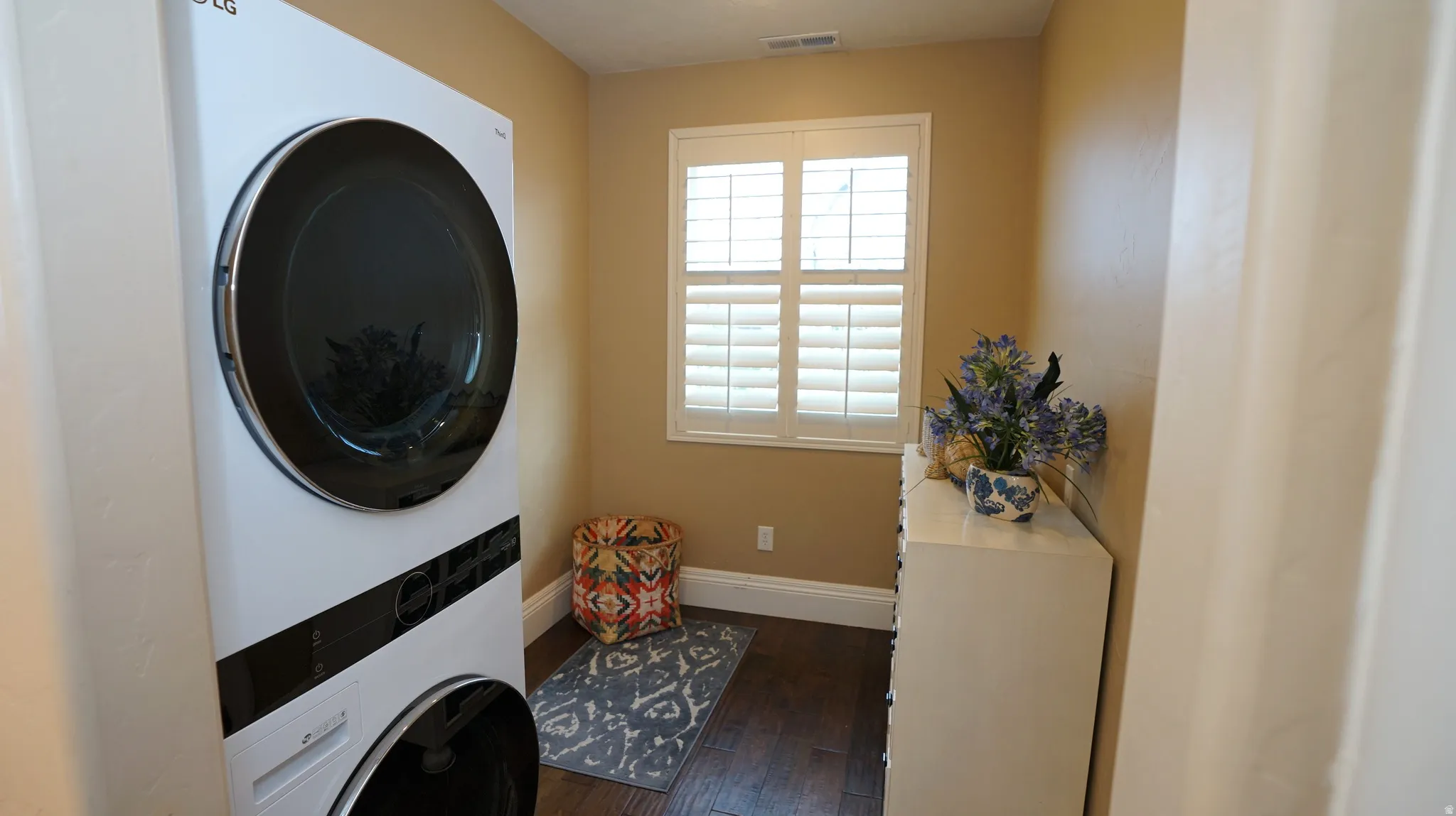 Laundry area featuring stacked washer and dryer unit, plantation shutters, and wood-finish flooring
