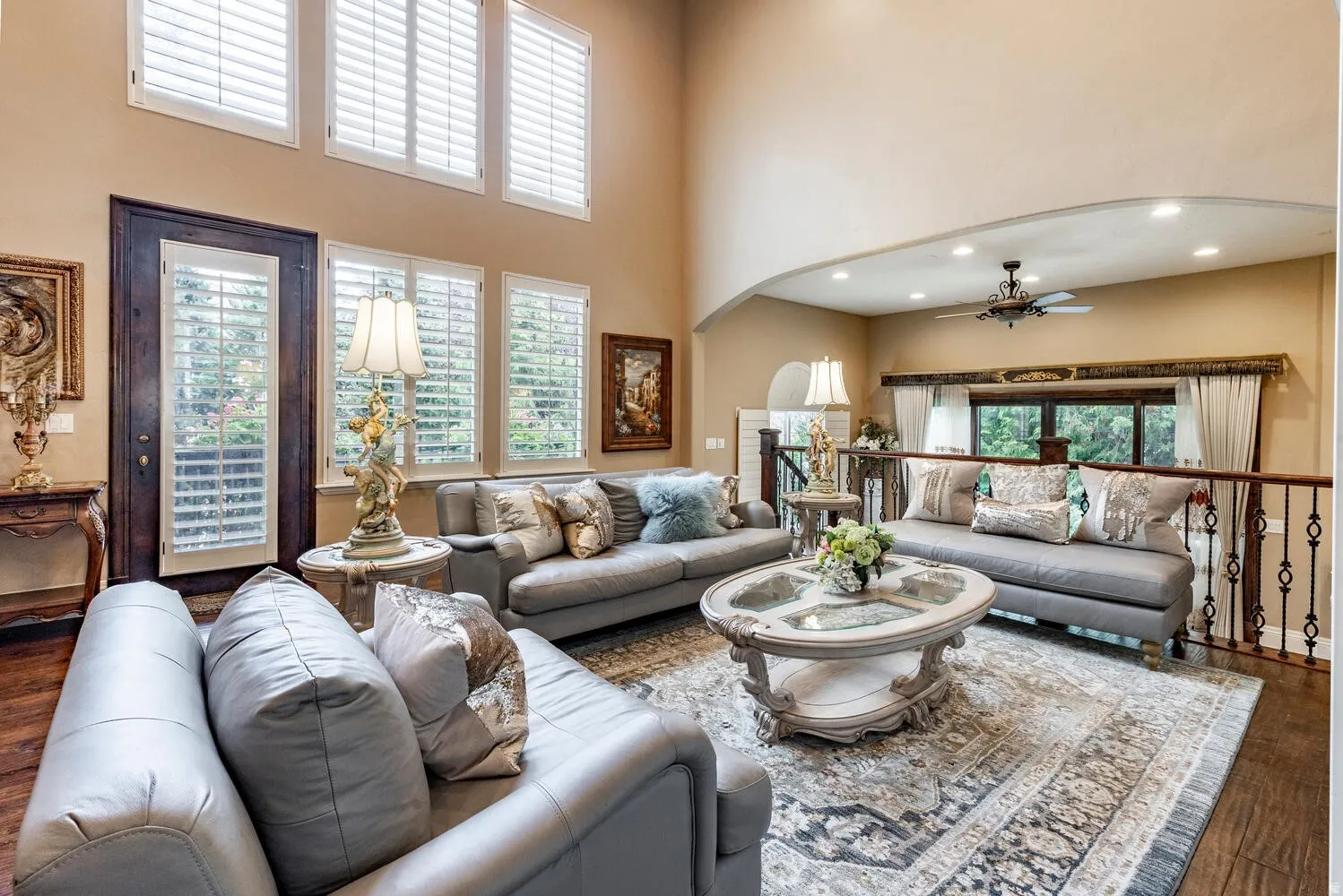 Double-height ceilings, multiple windows with white plantation shutters, dark wood-finish flooring, and an arched architectural opening