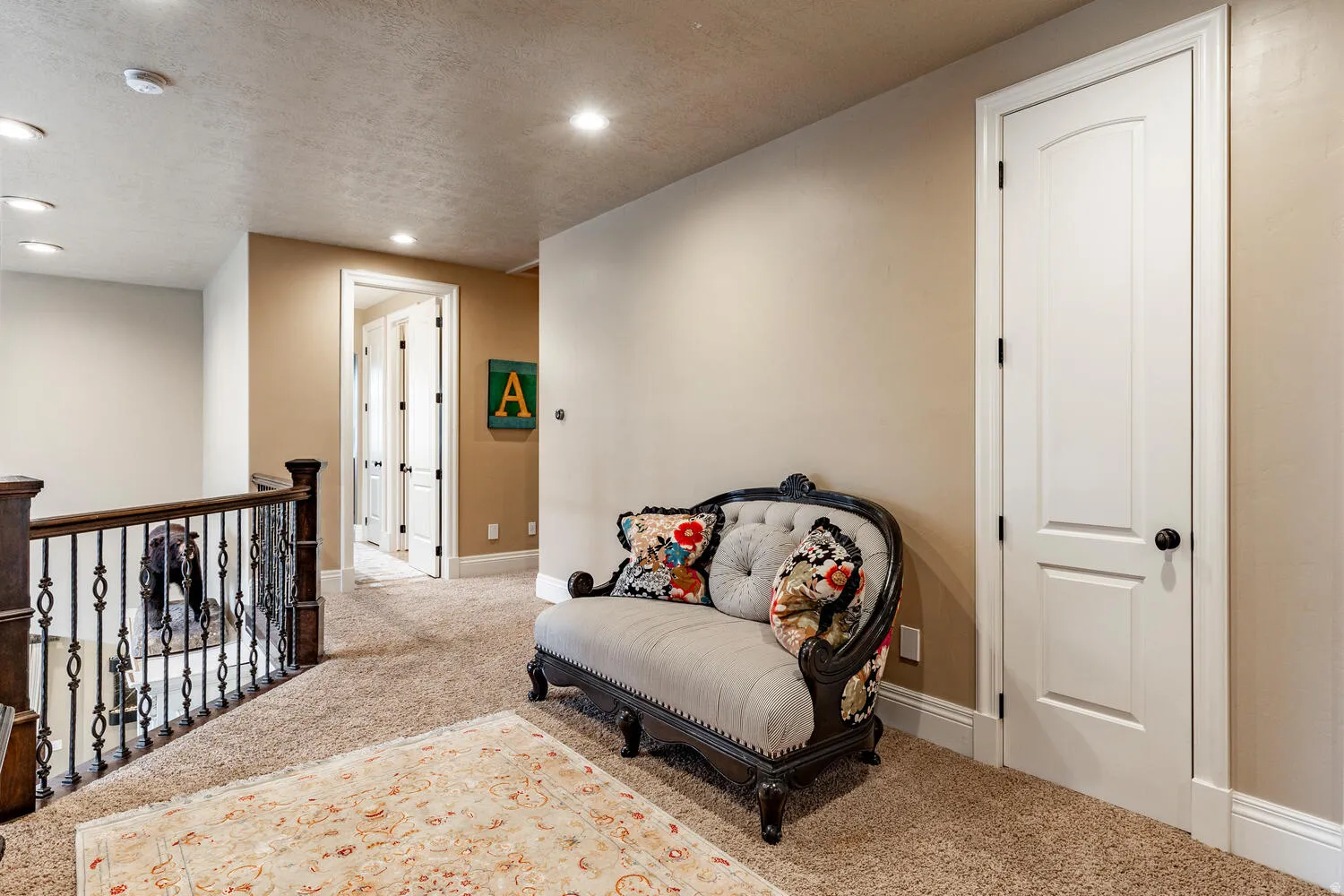 Carpeted landing featuring recessed lighting, a dark wood newel post, and wrought iron balusters