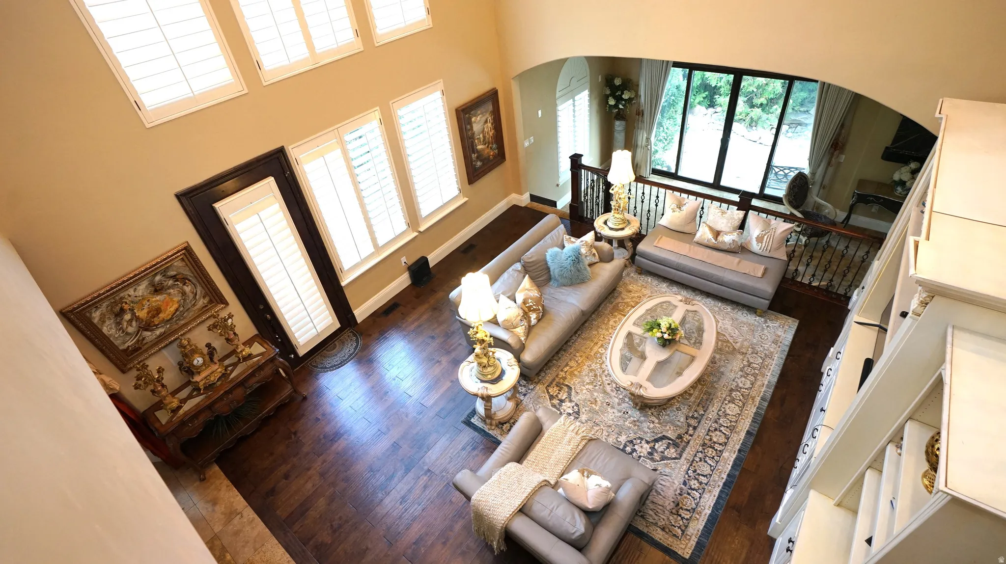 High ceilings, wood-finish flooring, multiple windows with plantation shutters, arched doorway, and white painted balusters
