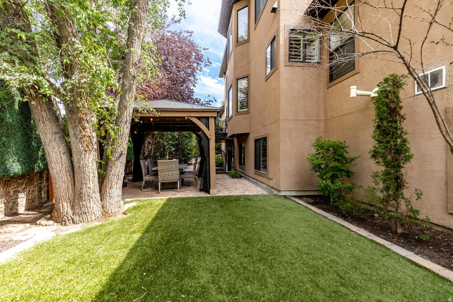 Backyard featuring artificial turf, a paved patio, and a built-in gazebo with string lighting