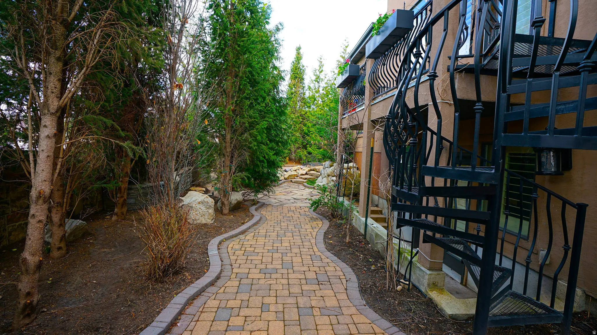 Paved walkway with stone edging, mature trees, and natural rock landscaping