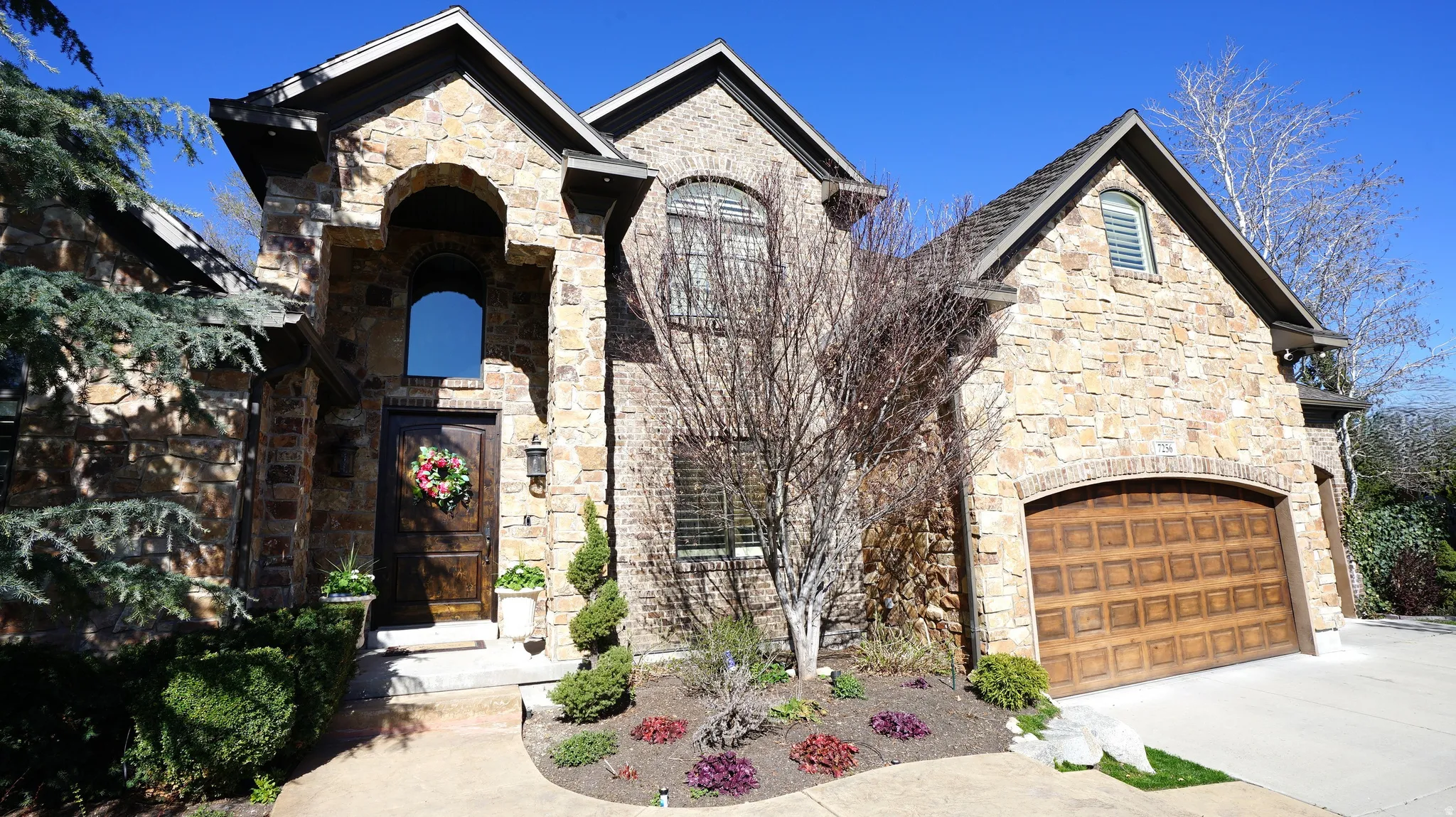 Stone facade residence featuring an arched entryway, gabled rooflines, and a wood-finish garage door