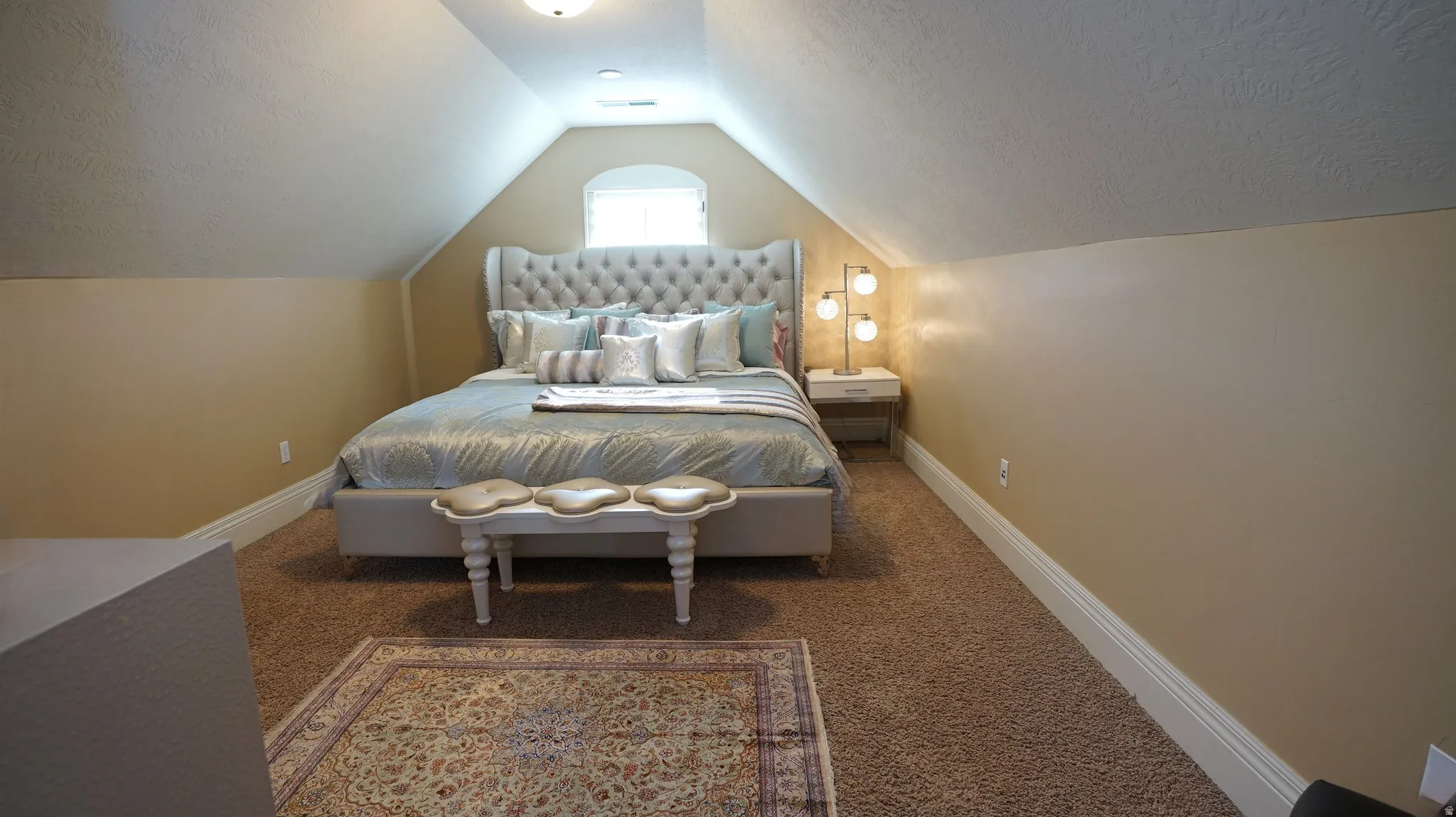 Vaulted ceiling, arched window, wall-to-wall carpeting, and white baseboards