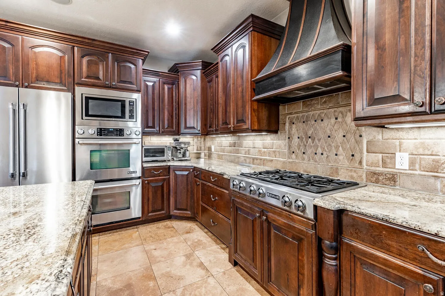 Dark wood cabinetry, stainless steel appliances, a built-in oven and microwave, stone countertops, and a decorative tile backsplash