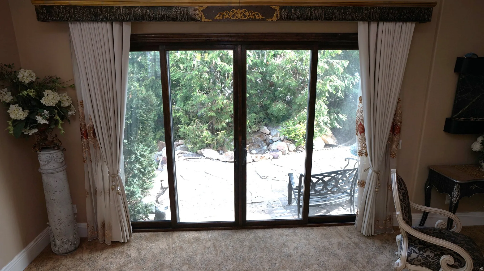 Sliding glass door opening to a paved patio, surrounded by mature greenery