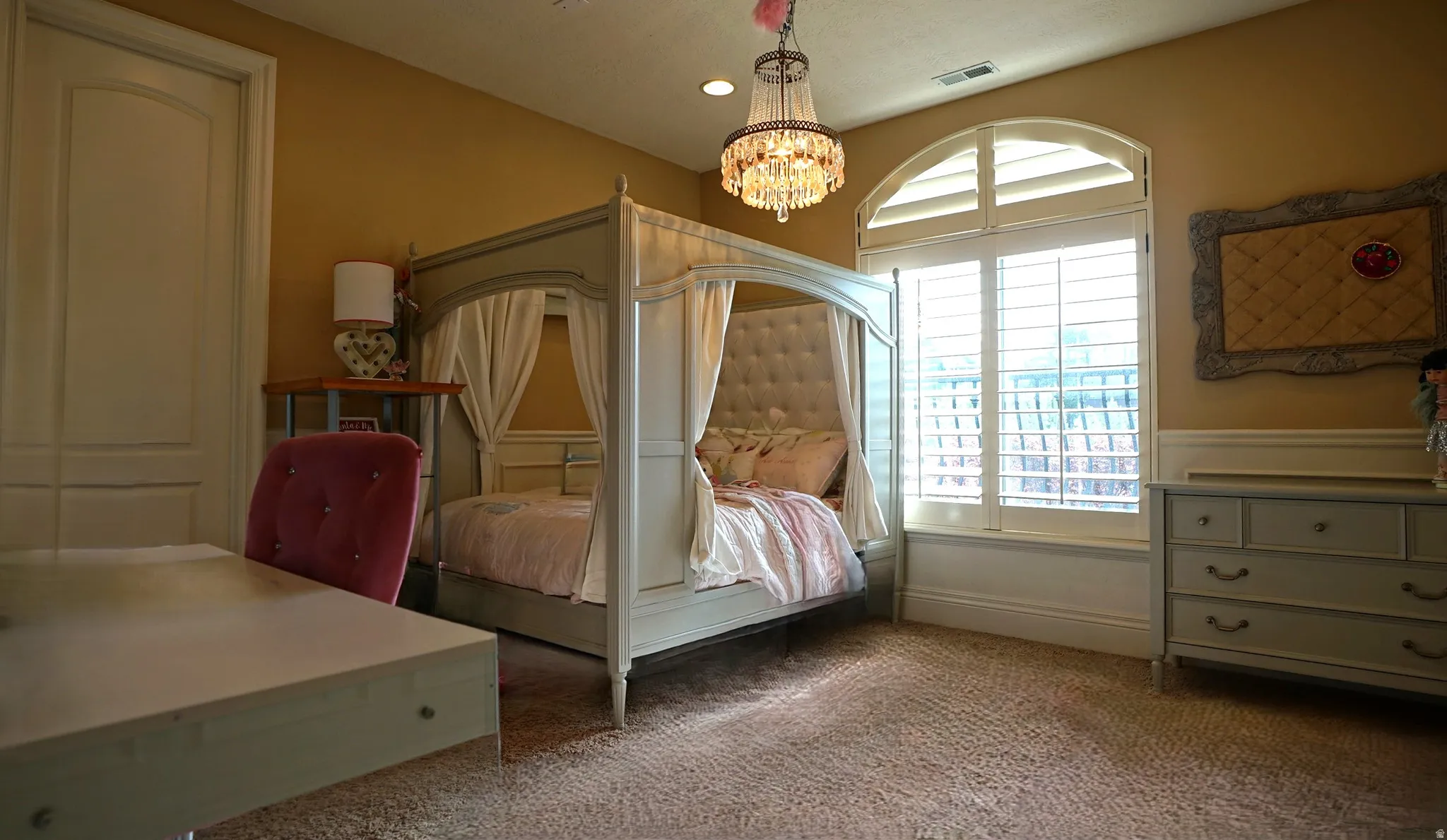 Arched window with plantation shutters, wainscoting, and a crystal chandelier