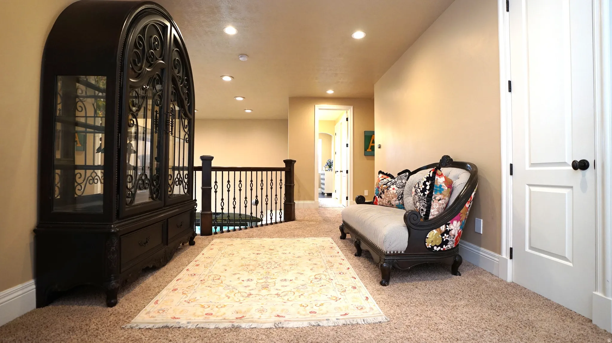 Carpeted flooring, recessed lighting, white interior doors with black hardware, and wrought iron railing