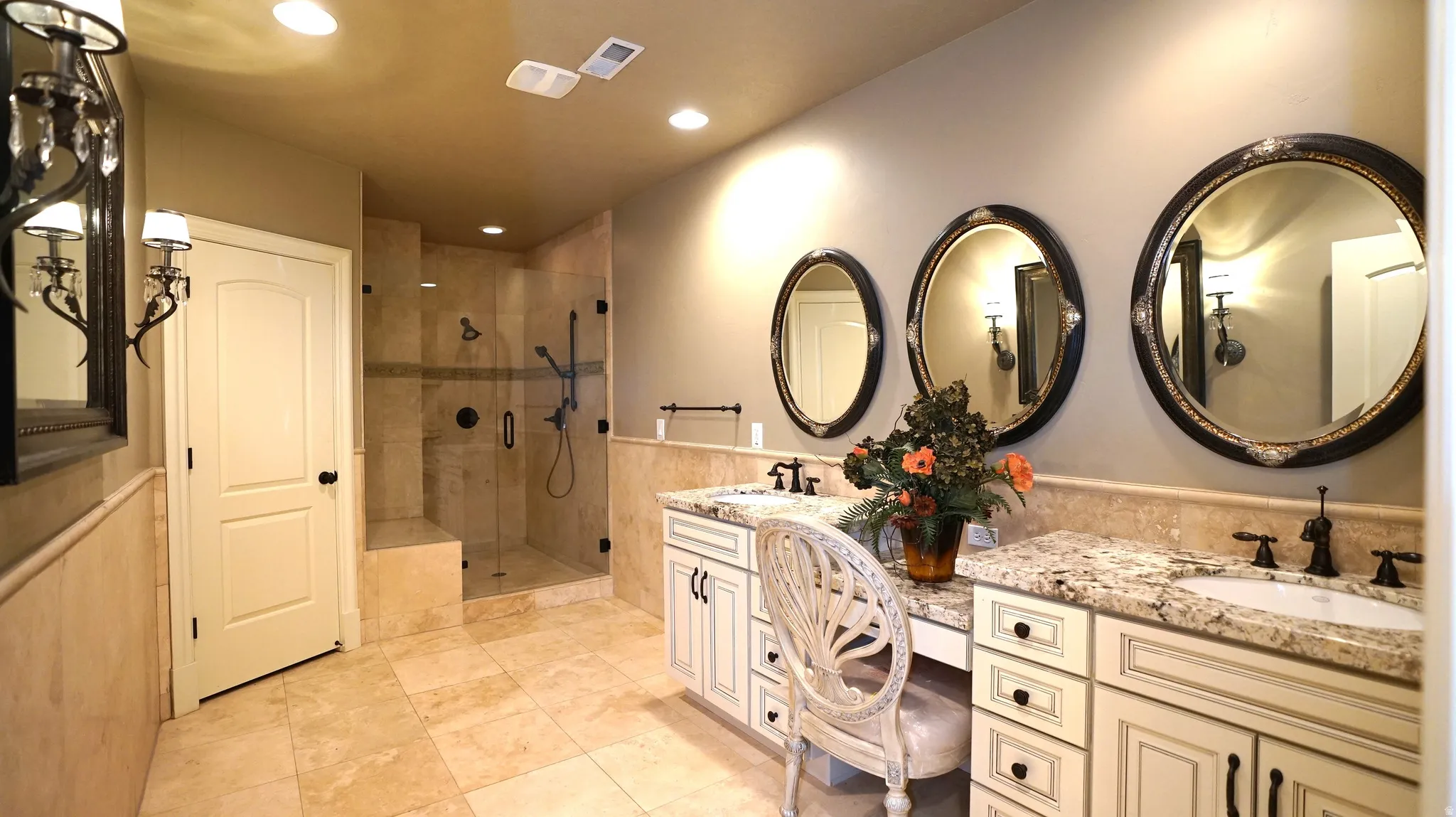 Tiled bathroom with a glass-enclosed shower, dual vanity sinks, and multiple framed mirrors