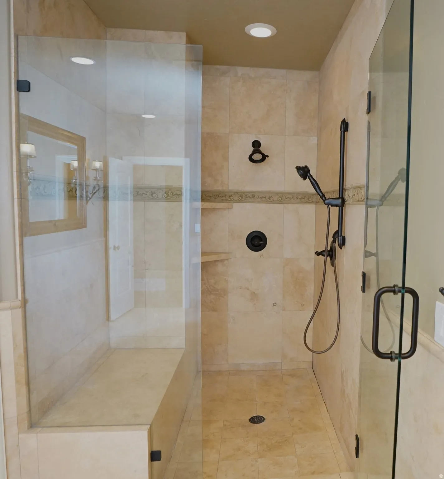Glass-enclosed shower with a built-in bench, natural stone tile, and oil-rubbed bronze fixtures