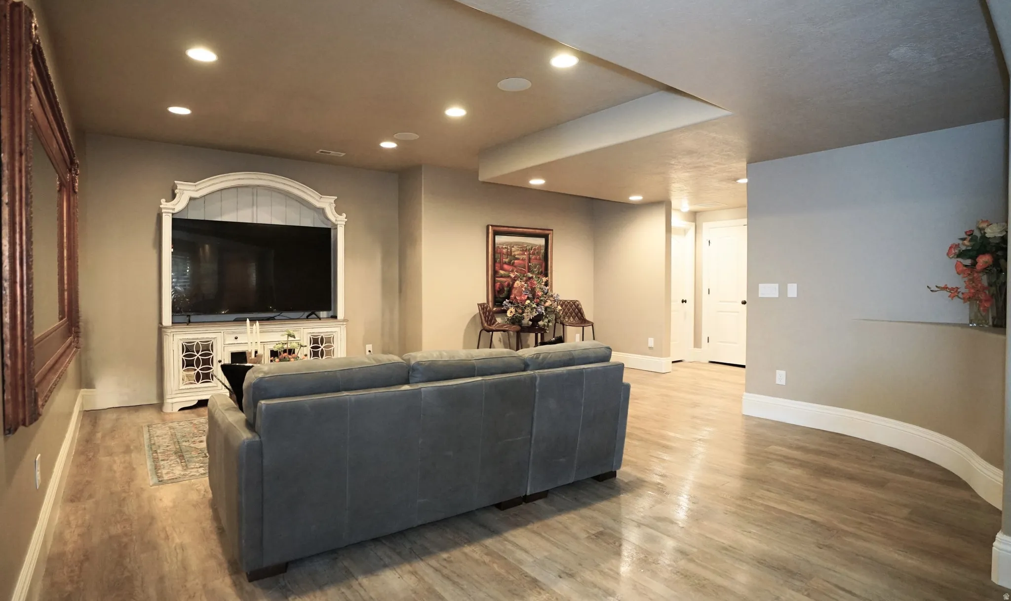 Recessed lighting, wood-finish flooring, built-in media console, white trim, and a curved wall detail