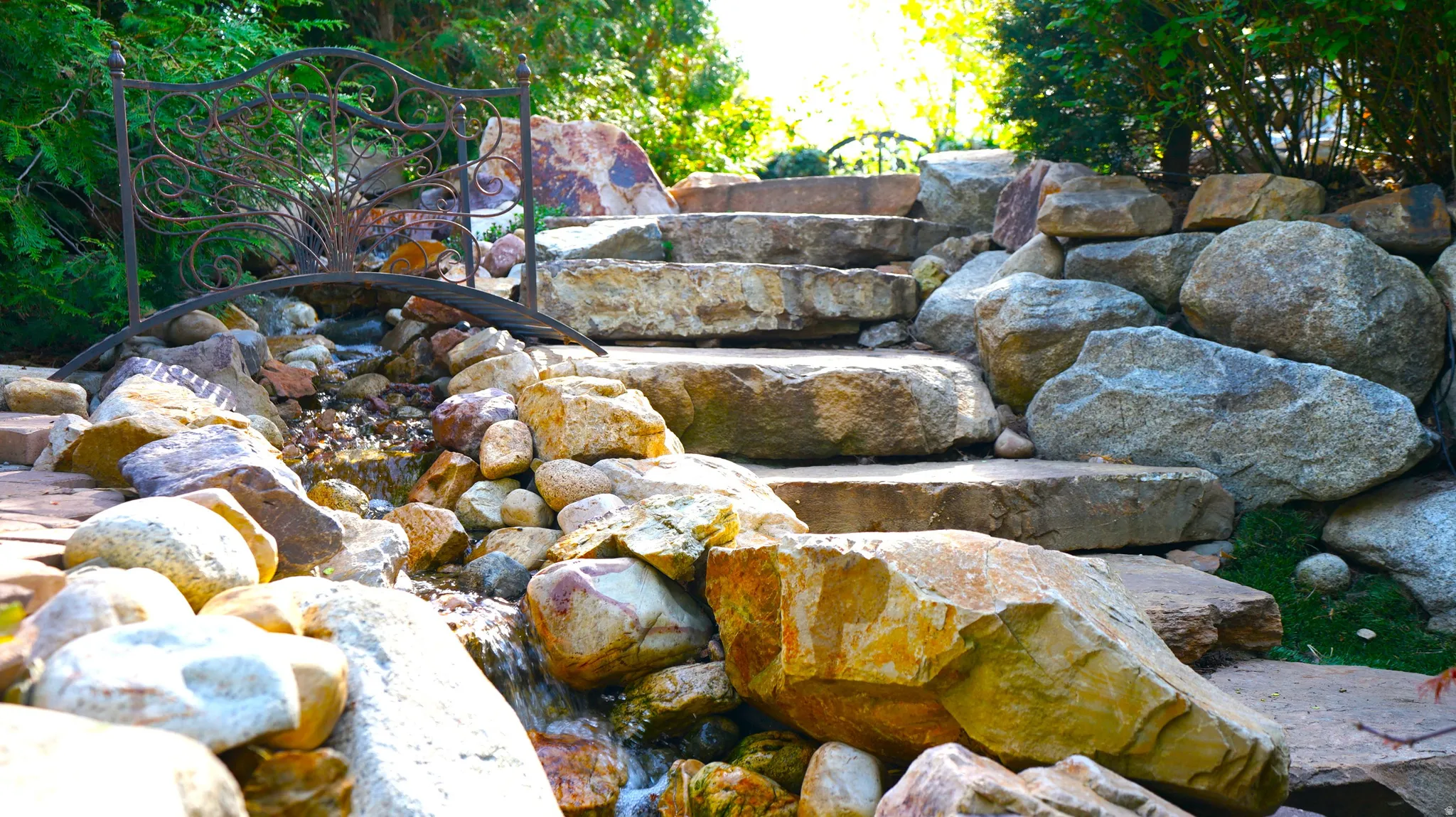Natural stone steps, ornamental metal bridge, and a rock-lined water feature