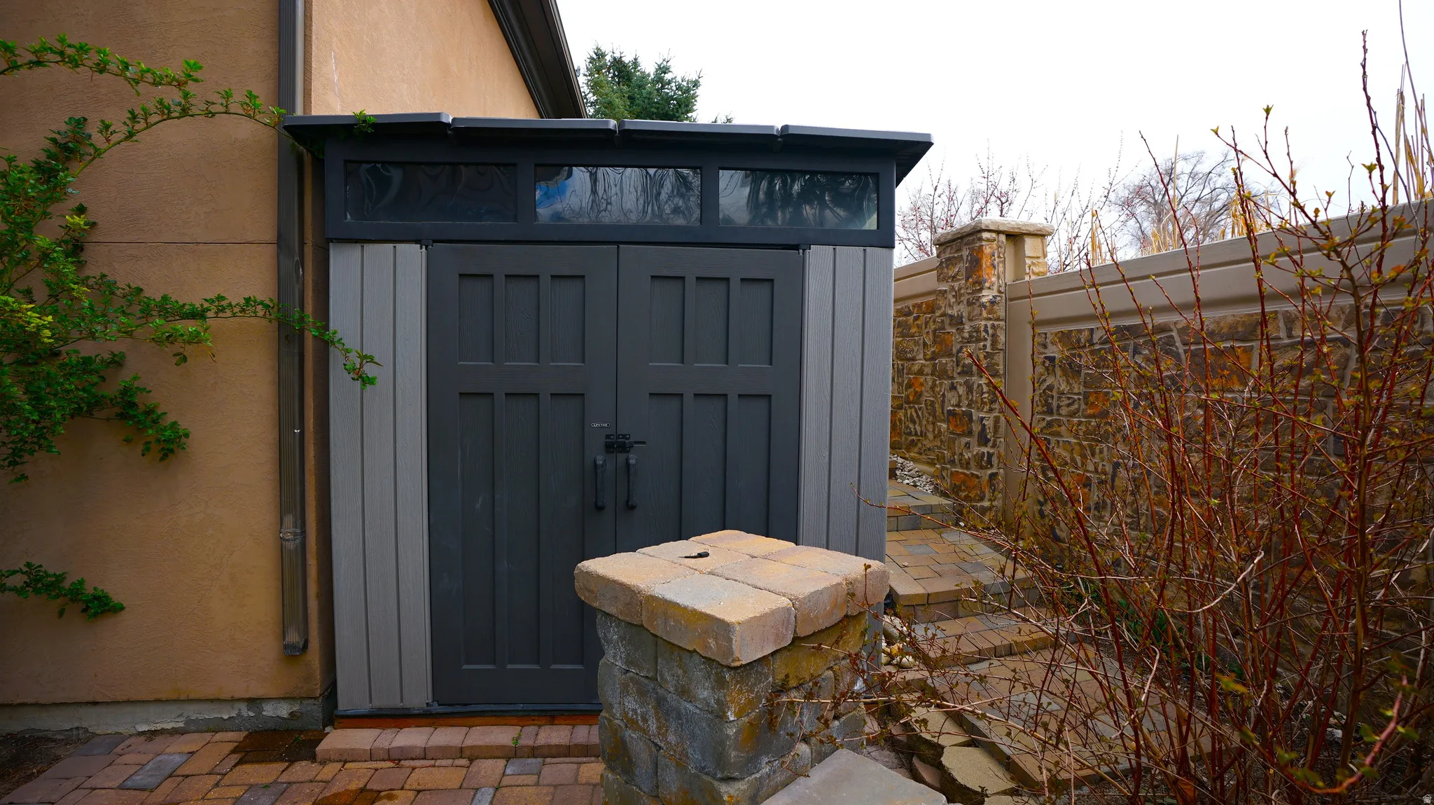 Custom storage shed with transom windows, stone accents, and paved path