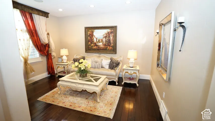 Hardwood flooring throughout, recessed ceiling lighting, wall-mounted sconce lighting, and a large window with custom window treatments