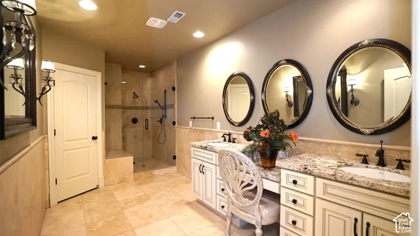 Tiled bathroom with a glass-enclosed shower, dual vanity sinks, and multiple framed mirrors