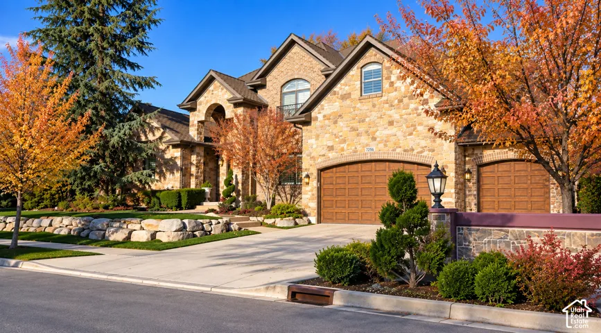 Stone exterior with arched entryways, wood-finish garage doors, and mature landscaping
