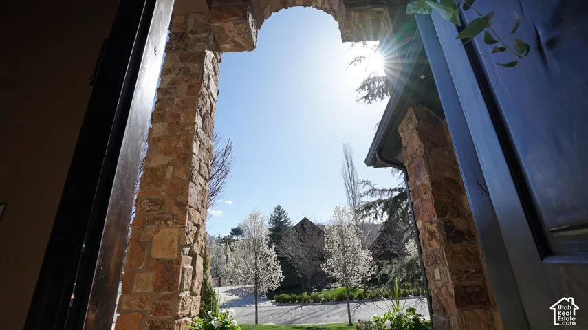 Archway entry with stone masonry, dark wood door, lush landscaping, and flowering trees