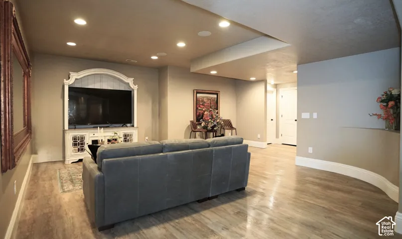 Recessed lighting, wood-finish flooring, built-in media console, white trim, and a curved wall detail